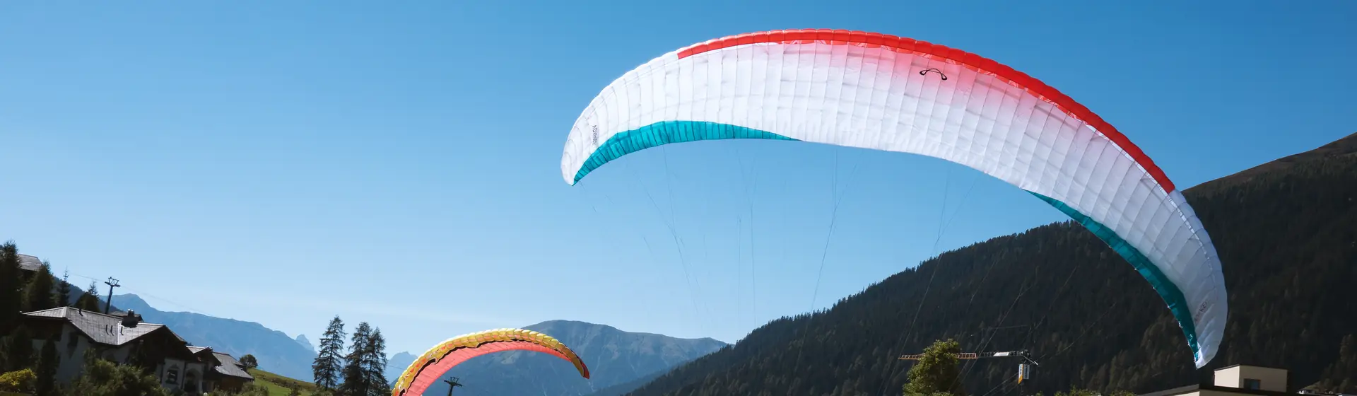 Bike & Fly in Davos: Tandem-Gleitschirm über der Davoser Bergwelt und Mountainbiker auf einem Trail