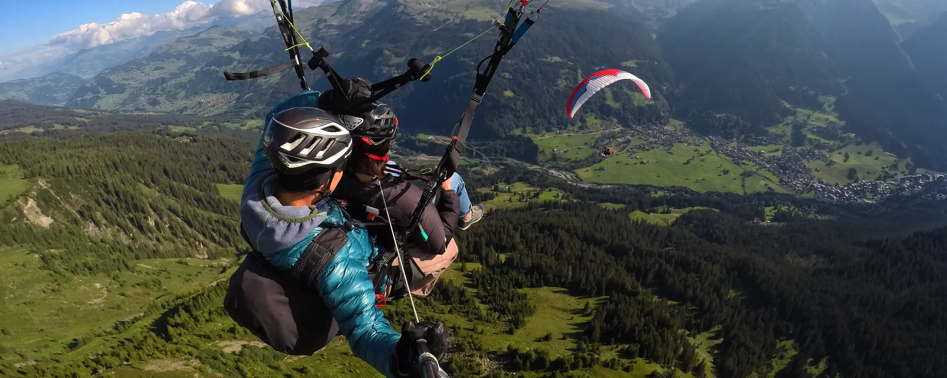 Tandempilot und Passagier beim Gleitschirm-Tandemflug über Davos, dahinter ein zweiter Tandemschirm über dem Tal