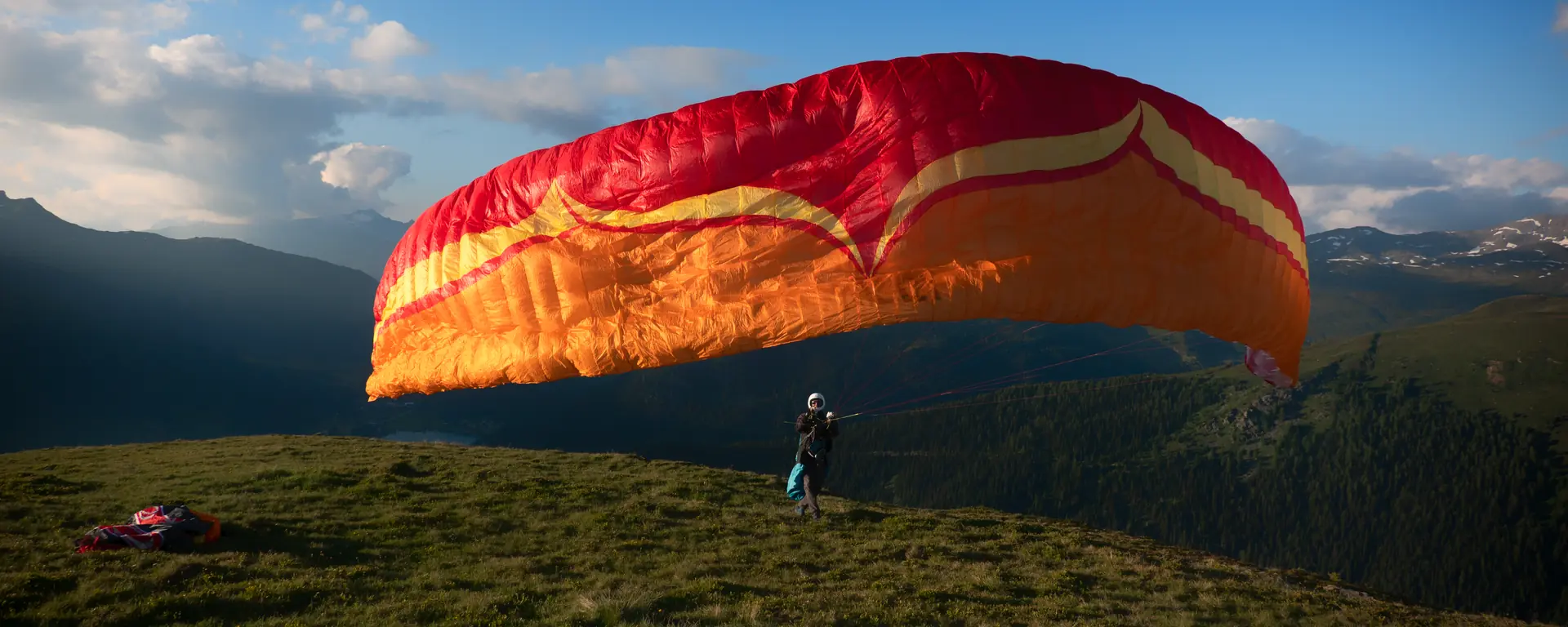 Pilot zieht den Gleitschirm auf einer Bergkuppe hoch über Davos auf, im Abendlicht mit Blick Richtung Davosersee