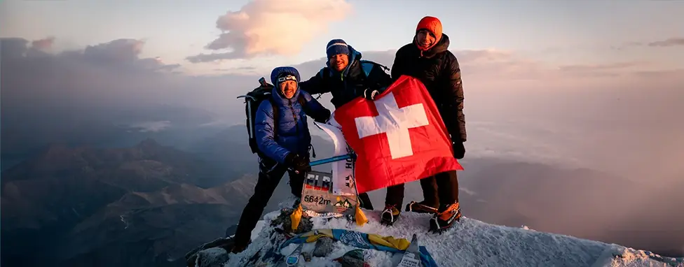 Three Air-Davos mountaineers with a Swiss flag on the summit of Mount Elbrus (5,642 m) at sunrise